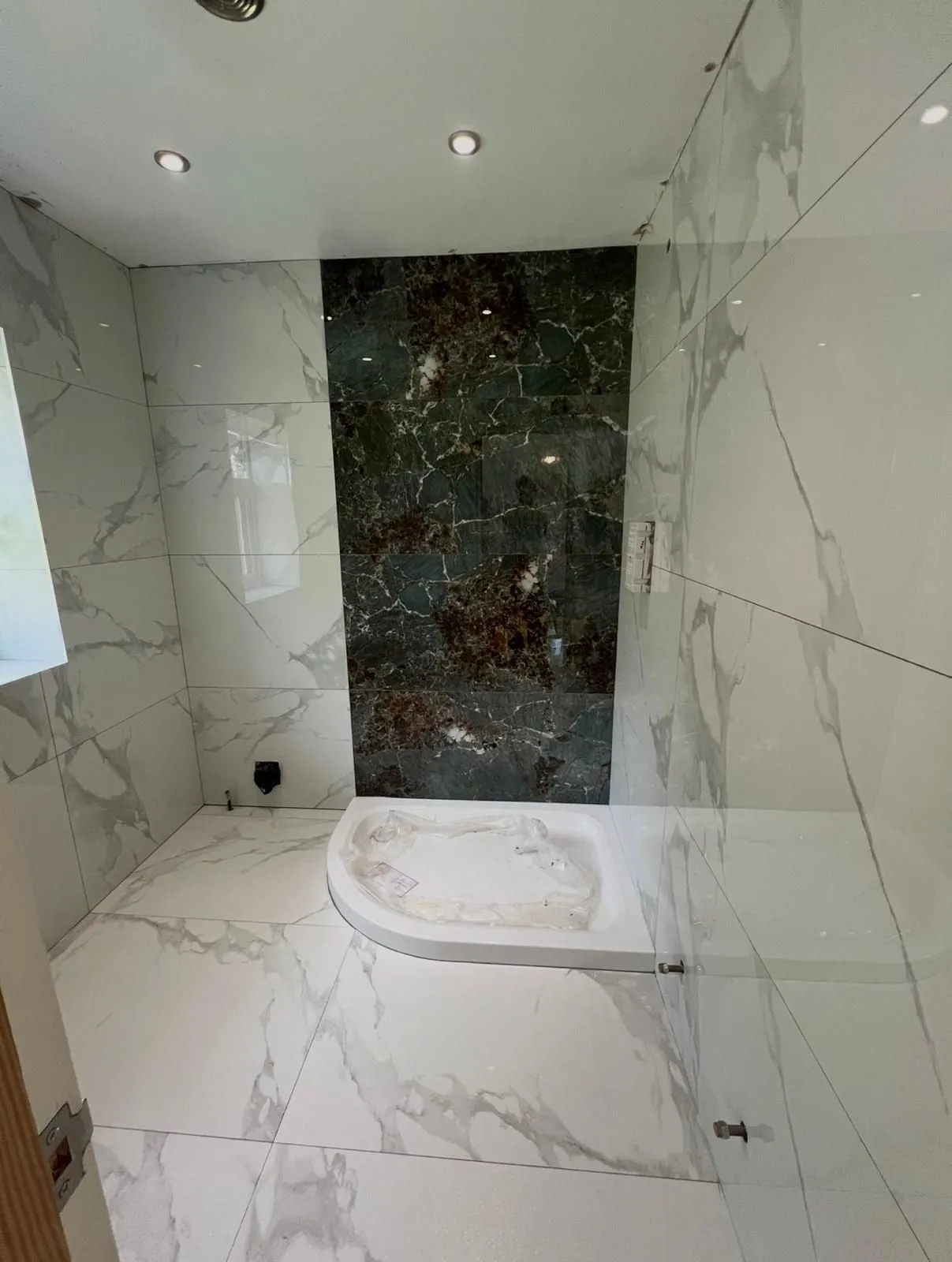 White calacatta-effect walls and floor around a stone shower tray with a dark marble feature panel