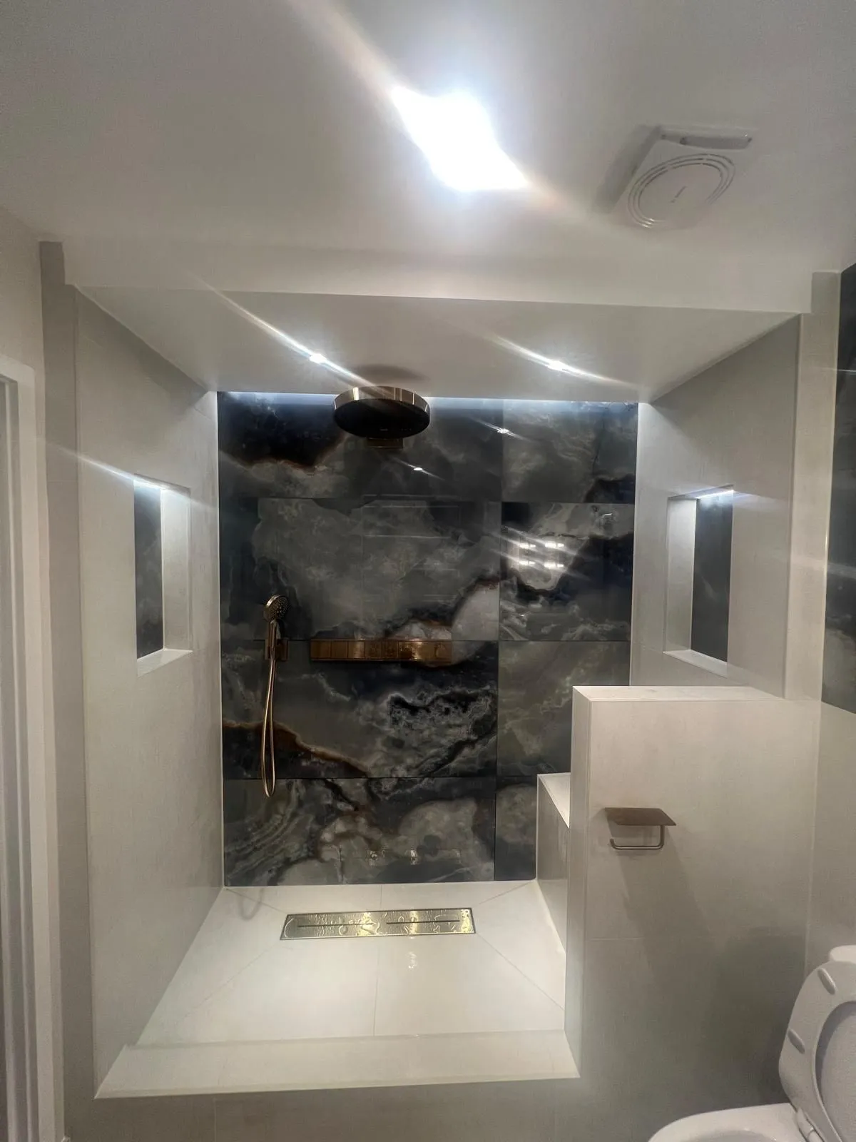 Walk-in shower with a single onyx-effect feature slab and linear drain