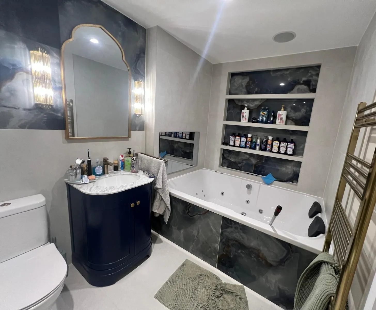 Navy vanity under an arched brass mirror, with onyx-effect tiles and recessed shelving