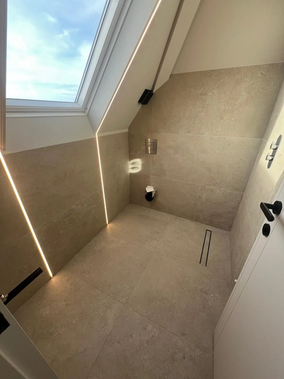 Sloped-ceiling shower room in warm porcelain with LED lighting lines