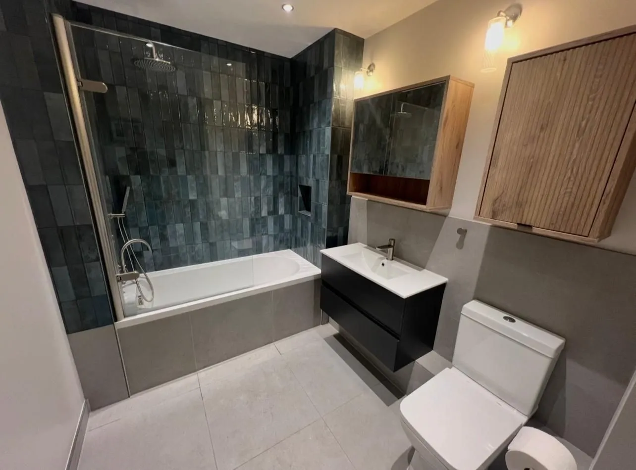 Bathroom with green handmade-style wall tiles over the bath and a black vanity