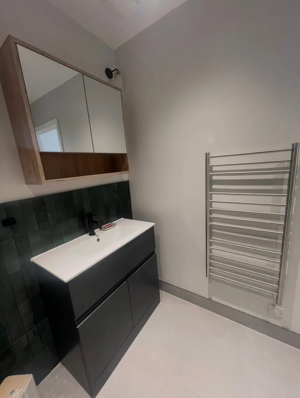 Black vanity and mirror cabinet against green handmade-style tiles